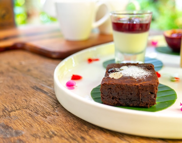 Brownie de chocolate cubierto con almendras Colocado en un plato blanco sobre una mesa de madera.