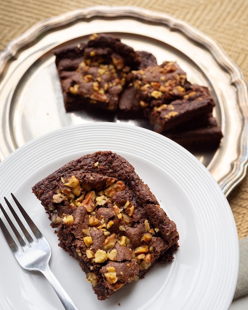 Foto brownie de chocolate com nozes servido em um prato branco com garfo