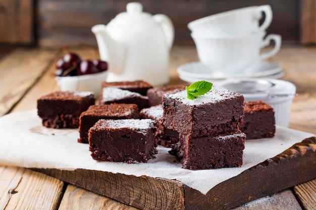 Brownies de chocolate con azúcar en polvo y cerezas sobre una superficie de madera oscura. Enfoque selectivo.