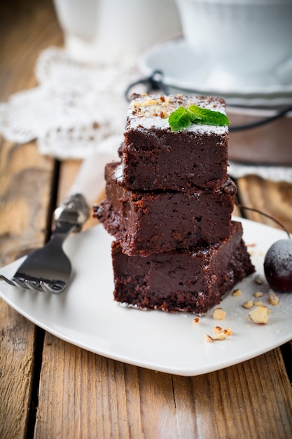 Brownies de chocolate con azúcar en polvo y cerezas sobre una superficie de madera oscura. Enfoque selectivo.