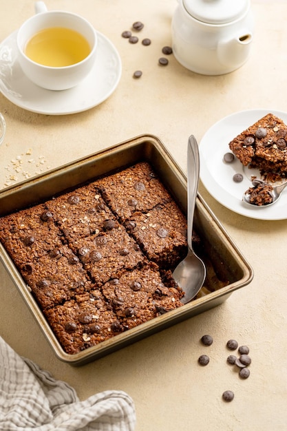 Brownies com lascas de chocolate e aveia em flocos servidos com uma xícara de chá em fundo rosa