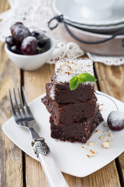 Brownies de chocolate com açúcar de confeiteiro e cerejas em madeira escura