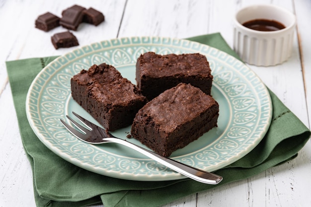 Brownies em um prato verde com pedaços de chocolate e calda sobre mesa de madeira branca