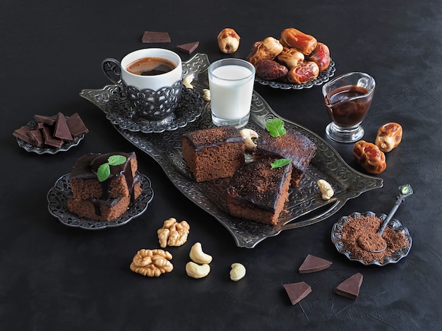 Brownies mit Datteln, Milch und Kaffee liegen auf einer schwarzen Oberfläche. Festlicher Ramadan Hintergrund