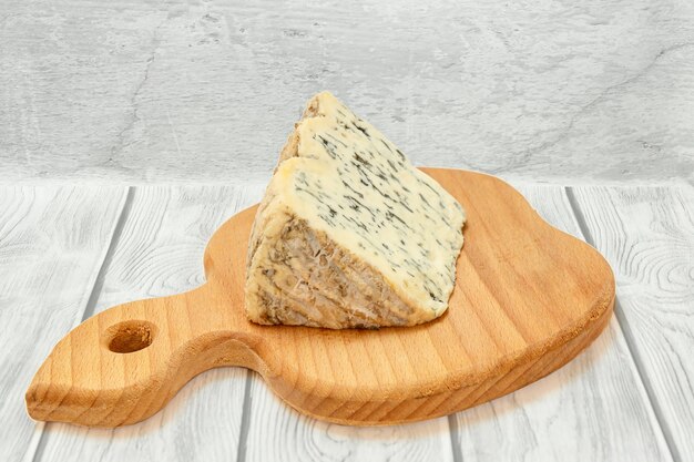 Bruch von Fourme d'Ambert, einem halbharten französischen Blauschimmelkäse auf einem Holzbrett mit grauer Holzoberfläche