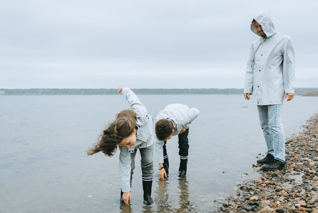 Bruder mit Schwester haben Spaß im Meer im Regenmantel