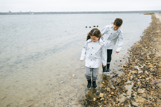 Bruder mit Schwester haben Spaß im Meer im Regenmantel