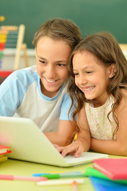 Bruder und Schwester benutzen einen Laptop, während sie zu Hause am Tisch sitzen