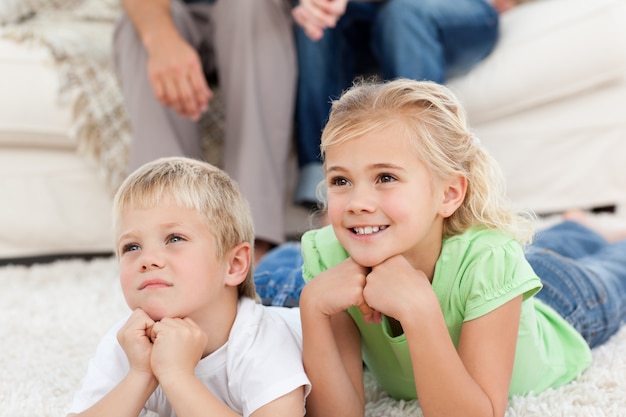 Bruder und Schwester, die mit ihren Eltern auf dem Boden fernsehen