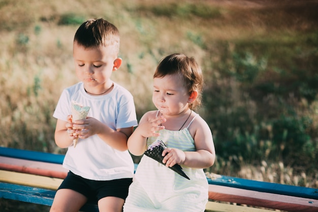 Bruder und Schwester essen Eis auf der Bank auf dem Spielplatz ist sehr süß