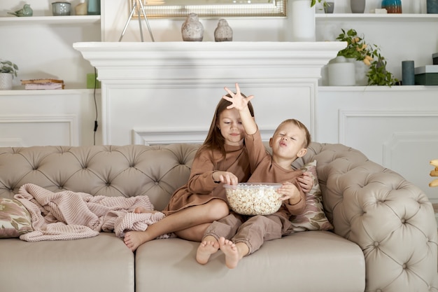 Bruder und schwester essen popcorn, das zu hause auf der couch sitzt