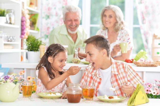 Bruder und Schwester frühstücken zusammen mit ihren Großeltern im Hintergrund