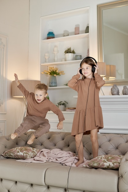 Bruder und Schwester haben Spaß zu Hause und springen auf die Couch. Kinder tanzen und hören Musik mit Kopfhörern