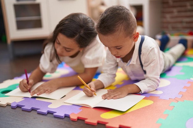 Foto bruder und schwester liegen im kindergarten auf dem boden und zeichnen auf papier