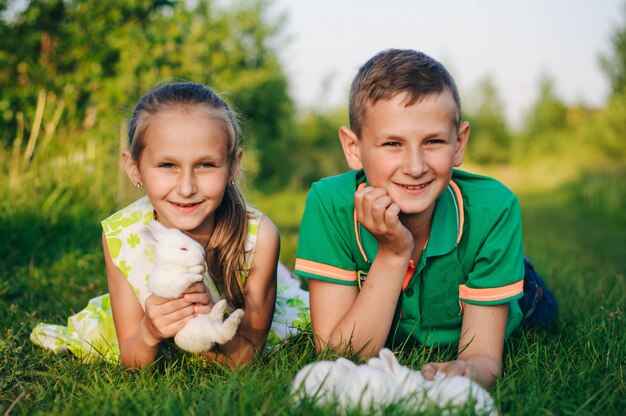 Bruder und Schwester liegen mit kleinen Kaninchen im Gras. Osterhase