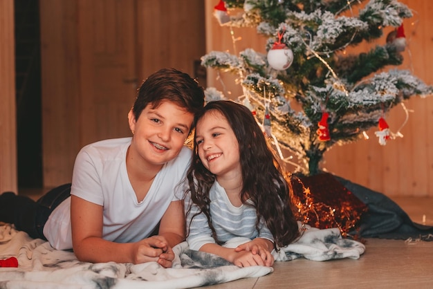 Bruder und Schwester liegen und lachen unter dem Weihnachtsbaum