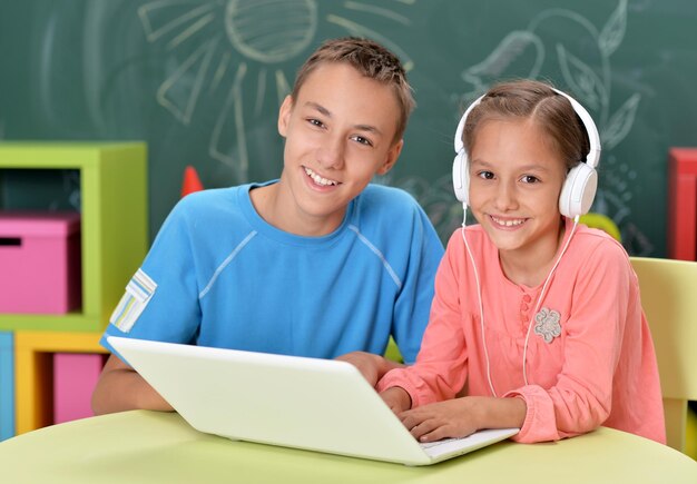 Bruder und Schwester mit Laptop weiß sitzend am Tisch Mädchen mit Kopfhörern