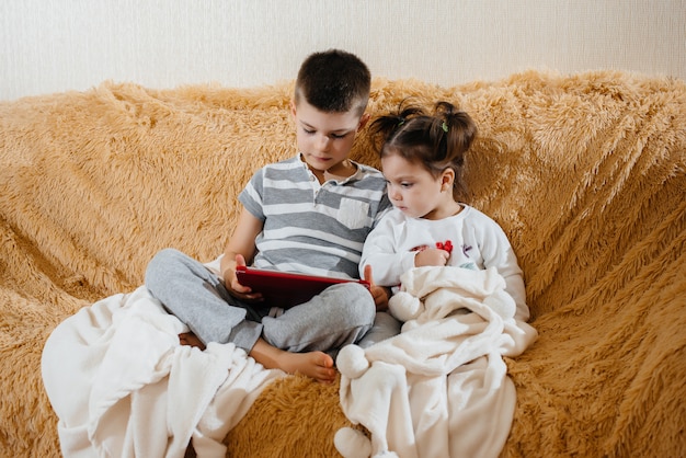 Bruder und Schwester spielen auf der Couch im Tablet.