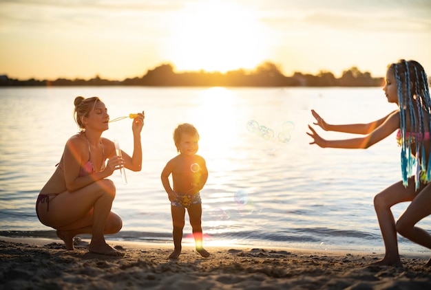 Bruder und Schwester spielen mit ihrer Mutter, die Seifenblasen auf dem See bläst