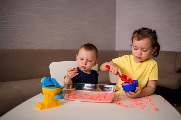 Bruder und Schwester spielen mit kinetischem Sand am Tisch im Raum. Sinnesentwicklungsspiele für Kinder zu Hause.