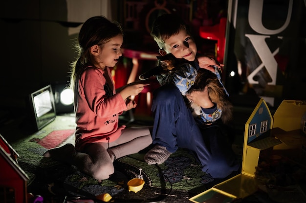 Bruder und Schwester spielen zu Hause mit Kätzchen während eines Stromausfalls mit alternativer Beleuchtung