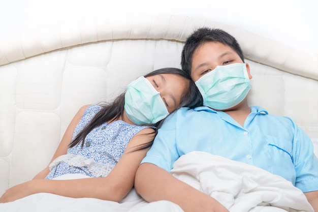 Bruder und Schwester tragen medizinische Gesichtsmaske auf dem Bett