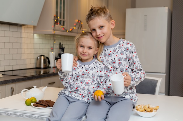 Bruder und Schwester trinken Milch oder Tee aus weißen Tassen in einer gemütlichen weißen Küche gesunder Snack