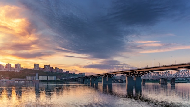 Brücke über den Jenissei-Fluss, Abendsonnenuntergang. Krasnojarsk, Russland. Panorama der Abendstadt, weicher Fokus.