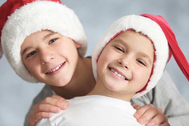 Brüder in Weihnachtsmützen auf grauem Hintergrund, Nahaufnahme