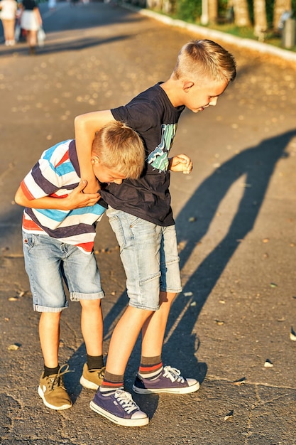 Brüder ringen auf Bürgersteig im öffentlichen Park Schuljungen amüsieren sich am Sommerabend im öffentlichen Park