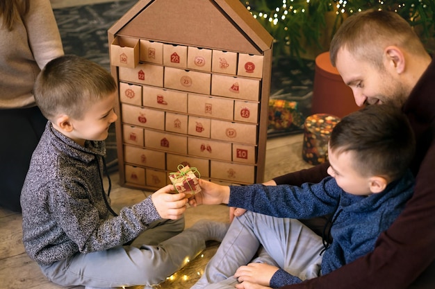 Brüder und Eltern öffnen den Adventskalender mit einer Geschenkbox