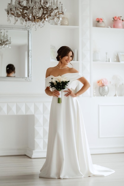 Brünette Braut in einem engen Hochzeitskleid in einem hellen Studio