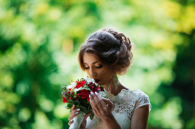 Brünette Braut in einem Hochzeitskleid und einem Blumenstrauß bei Sonnenuntergang im Park