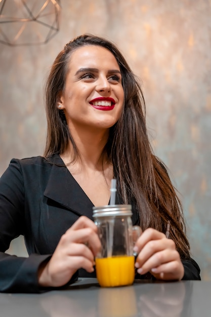 Brünette Frau, die in einem Kaffeegeschäft lächelt, das Orangensaft trinkt