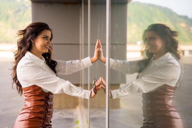 Brünette frau mit modischer pose in der stadt neben einem spiegelglas