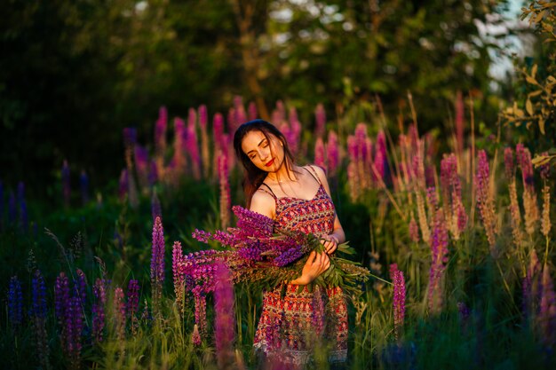 Brünette in einem Blumenfeld. Das Mädchen hält Lupinen lila