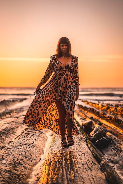 Brünette kaukasische Frau in einem Leopardenkleid am Meer und an den Felsen