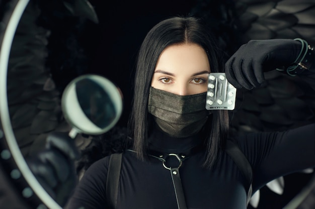 Foto brünette trägt eine schützende schwarze coronavirus-maske mit pillen und einer lupe