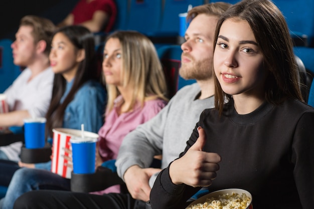 brünette zeigt daumen hoch beim filmen mit ihren freunden im lokalen kino