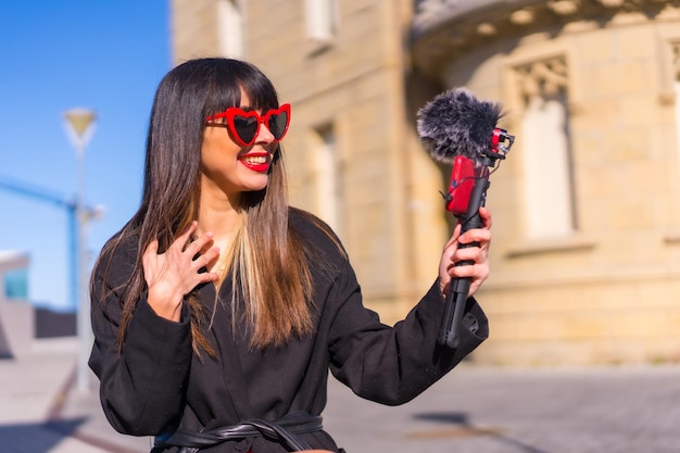 Brünettes kaukasisches Mädchen, das am Valentinstag einen Vlog mit roter Herz-Sonnenbrille macht und am Telefon und Mikrofon spricht