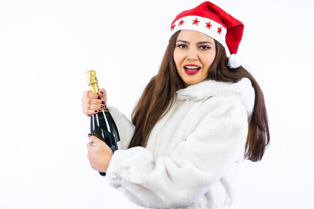 Brünettes lateinisches Mädchen zu Weihnachten mit weißem Hintergrund, mit Weihnachtsmütze mit Sternen, eine Flasche Champagner öffnend, Platz kopieren