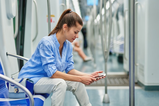 Brünettes Mädchen, das Handy an der U-Bahn benutzt.