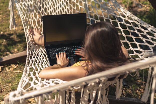 Brünettes Mädchen im gelben Badeanzug sitzt in der Hängematte mit Laptop, freiberuflich, Fernarbeit