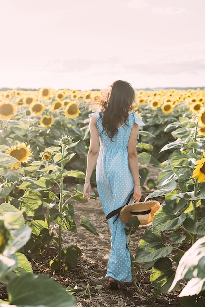 Brünettes Mädchen in einem eleganten Sommeroutfit und Strohhut in den Sonnenstrahlen auf einem Naturspaziergang