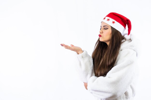 Brünettes Mädchen zu Weihnachten mit weißem Hintergrund, mit Weihnachtsmütze mit Sternen, Werfen und Kuss nach links, Kopierraum