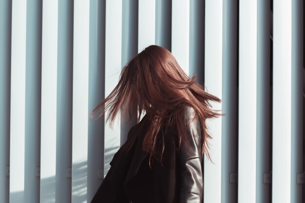 Brünettes Modell mit glänzenden langen Haaren, die im Wind flattern, auf der Straße spazieren gehen