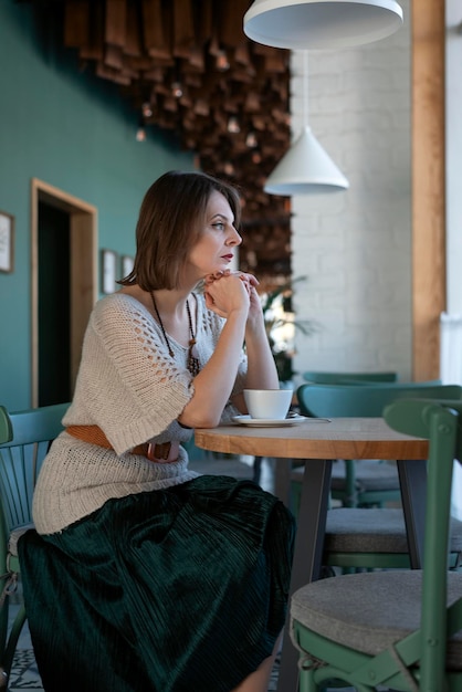 Brütende junge Frau sitzt am Tisch in einem leeren Café mit einer Tasse Kaffee Einsame Dame in der Cafeteria