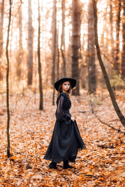 Bruja en el bosque de otoño. Una niña con un vestido largo negro camina en el bosque.
