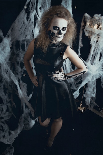 Bruja esqueleto de niña posando en las webs, Halloween. La bruja se prepara para las noches festivas de los muertos.