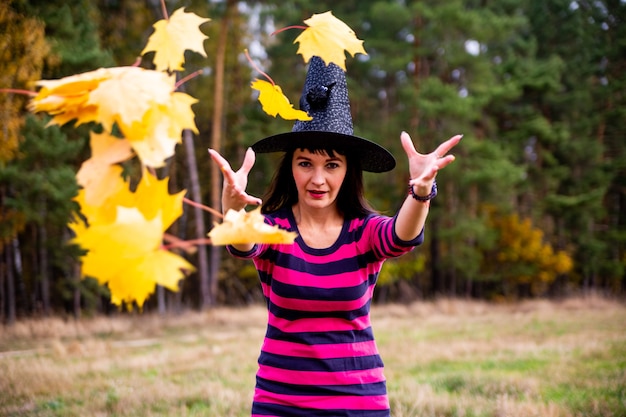 Bruja lanza hojas en el bosque de otoño mago de fiesta de disfraces de halloween